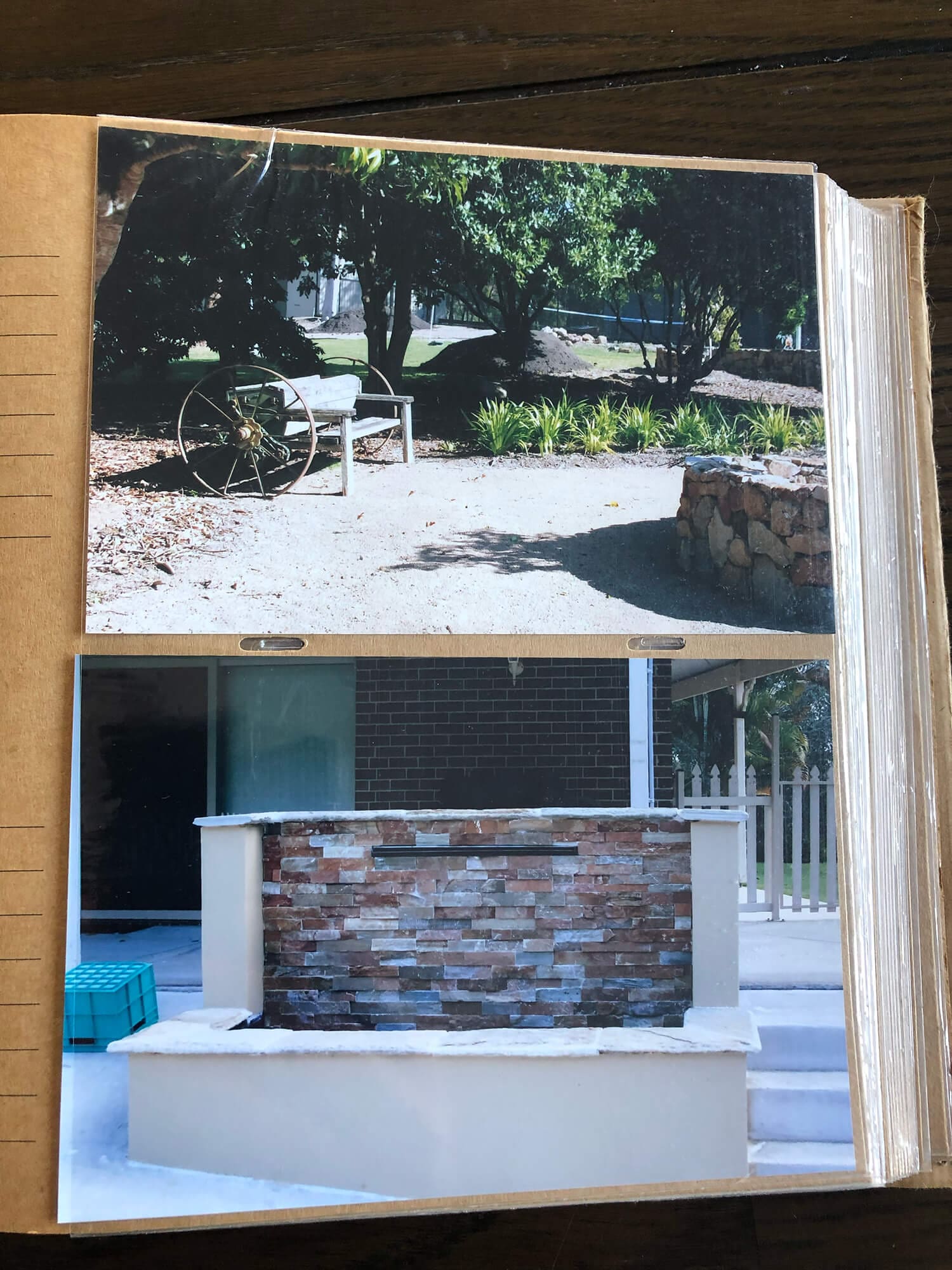 A photo album page contains two images. The top image shows an old wagon wheel and a wooden bench in a garden area. The bottom image displays a garden wall made of multicolored stacked stones with a modern patio setting in the background, reflecting the style often admired by Pool Builders Brisbane.