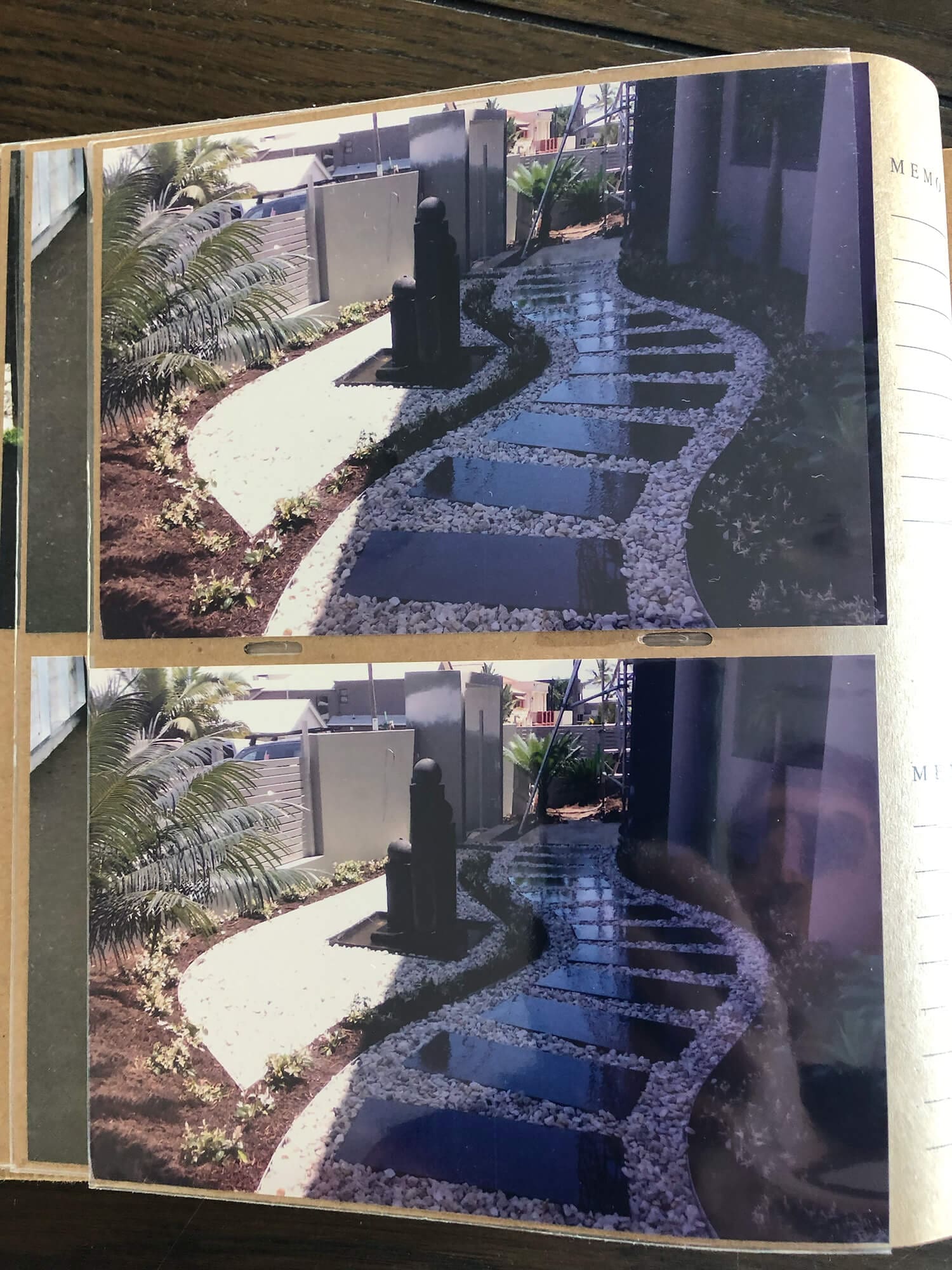 A photo album page displaying two similar photos of a landscaped garden path. The path, lined with stepping stones surrounded by gravel, curves through the garden. With lush green plants and a dark water feature at the center, it's an exemplar of Adella Pools’ work, top Pool Builders Brisbane offers.